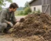 Une personne accroupie à côté d’un tas de fumier d’étable foncé mêlé de paille examine une poignée de matière.